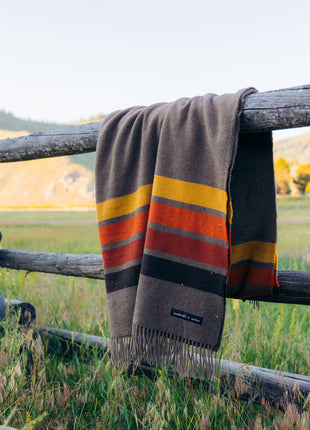 A cozy blanket hanging on a fence in a beautiful field.