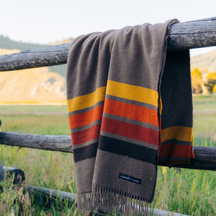 A cozy blanket hanging on a fence in a beautiful field.